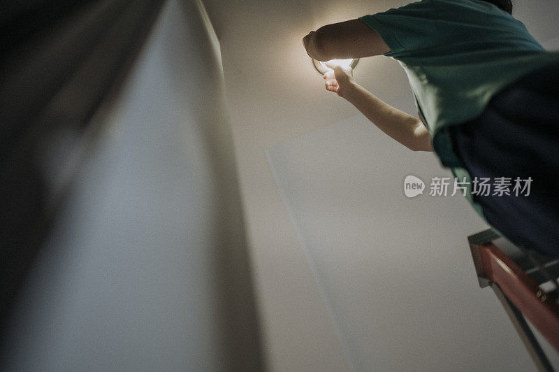 an asian chinese mid adult female changing light bulb in living room, apartment home